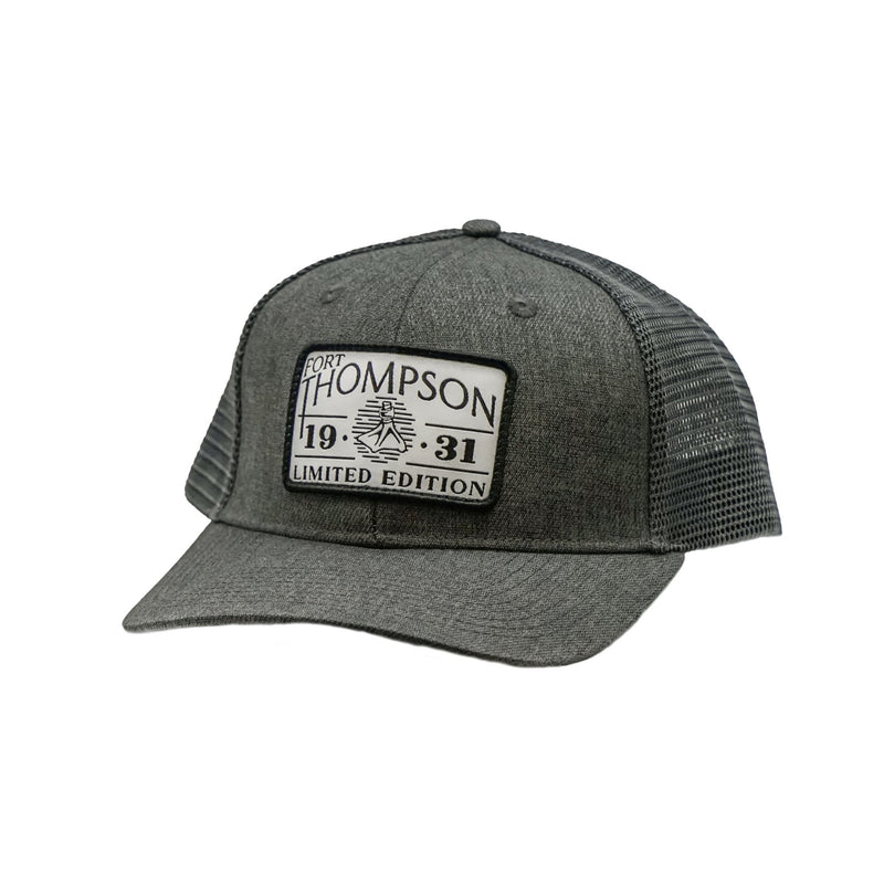 Load image into Gallery viewer, Fort Thompson White Rectangle Patch Trucker Style Hat in the color Charcoal with a rectangle patch that says &quot;Fort Thompson 1931 Limited Edition&quot; on the center of the hat.
